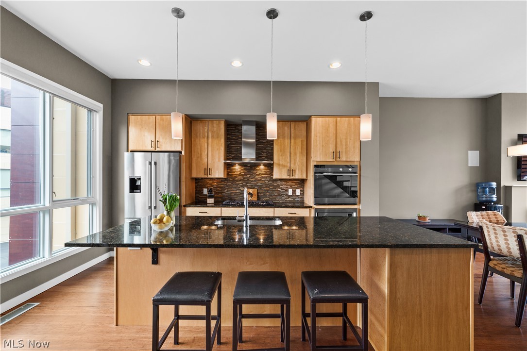 1868 Coltman Road Cleveland, OH 44106 - Photo 9 of 40 Kitchen featuring high quality fridge, a center island with sink, dark stone countertops, wall chimney exhaust hood, and a breakfast bar area