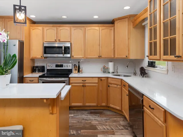 a large white kitchen with a large island oven a stove a sink a dining table and chairs with wooden floor