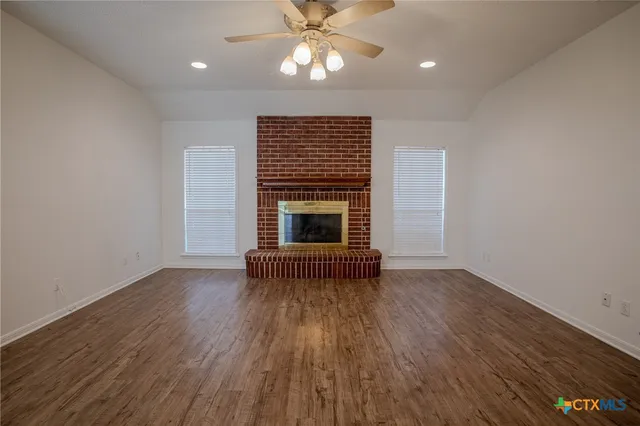 an empty room with wooden floor fireplace cabinet and windows