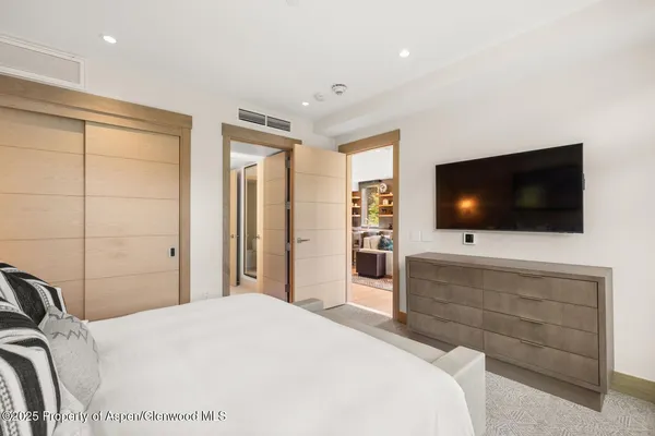 a spacious bedroom with a bed a couch and a flat tv screen on the dresser