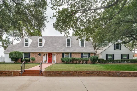 a view of brick house with a yard and large trees