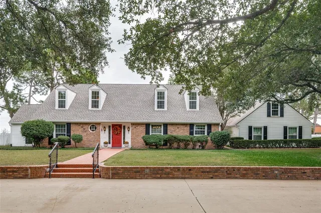 a view of brick house with a yard and large trees