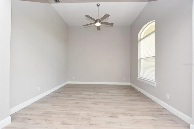 an empty room with wooden floor fan and windows