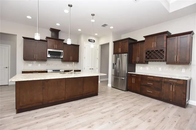 a large kitchen with stainless steel appliances kitchen island granite countertop a stove a sink dishwasher a refrigerator and a microwave oven with wooden floor