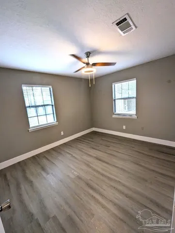 an empty room with wooden floor ceiling fan and windows