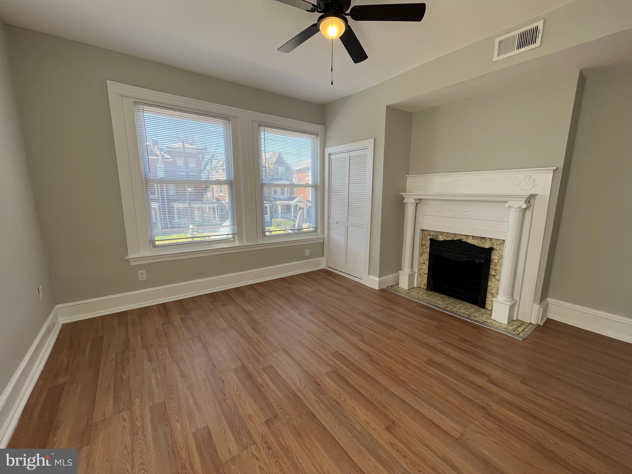 a view of an empty room with wooden floor fireplace and a window