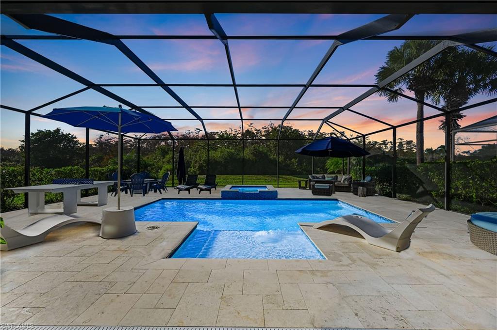 9121 Quartz Lane Naples, FL 34120 - Photo 1 of 36 Pool at dusk with a pool with connected hot tub, a lanai, a patio area, and a sunroom