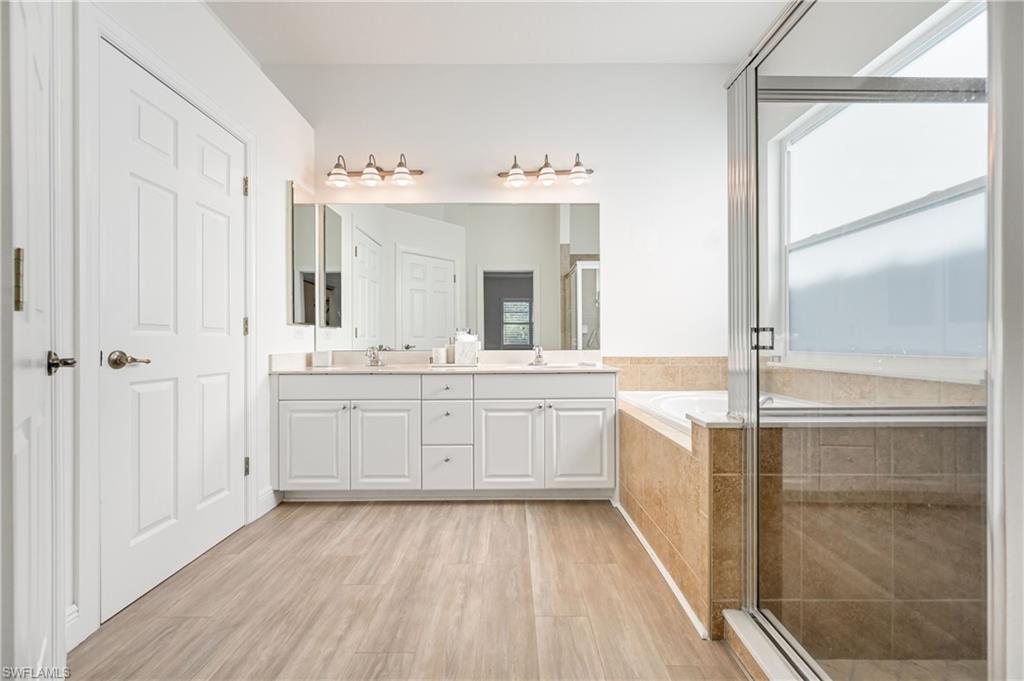 9121 Quartz Lane Naples, FL 34120 - Photo 14 of 36 Bathroom with double vanity, a shower stall, light wood-style flooring, a bath, and healthy amount of natural light