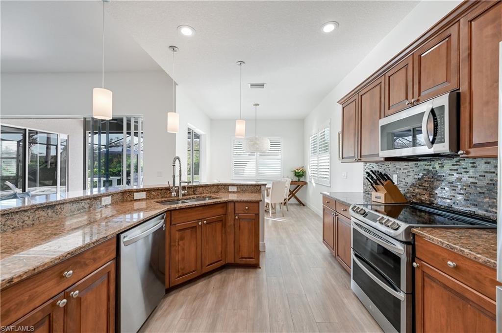 9121 Quartz Lane Naples, FL 34120 - Photo 4 of 36 Kitchen with brown cabinetry, appliances with stainless steel finishes, hanging light fixtures, light stone counters, and light wood-style floors