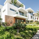 a view of a white building among the street with plants and brick walls