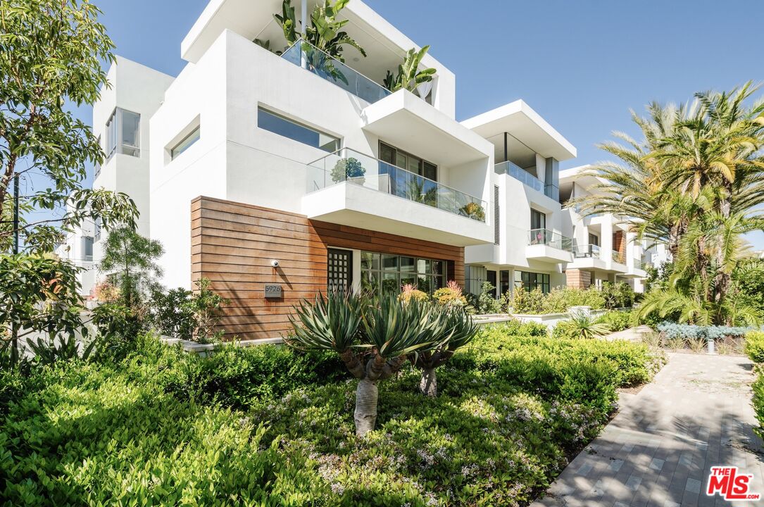 a view of a white building among the street with plants and brick walls