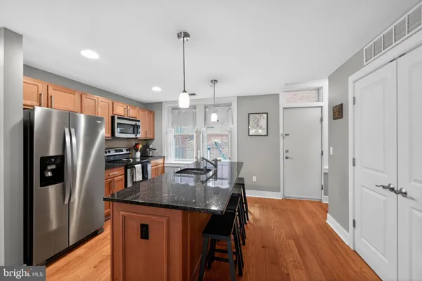 a kitchen with stainless steel appliances granite countertop a refrigerator a sink dishwasher a stove and a dining table with wooden floor