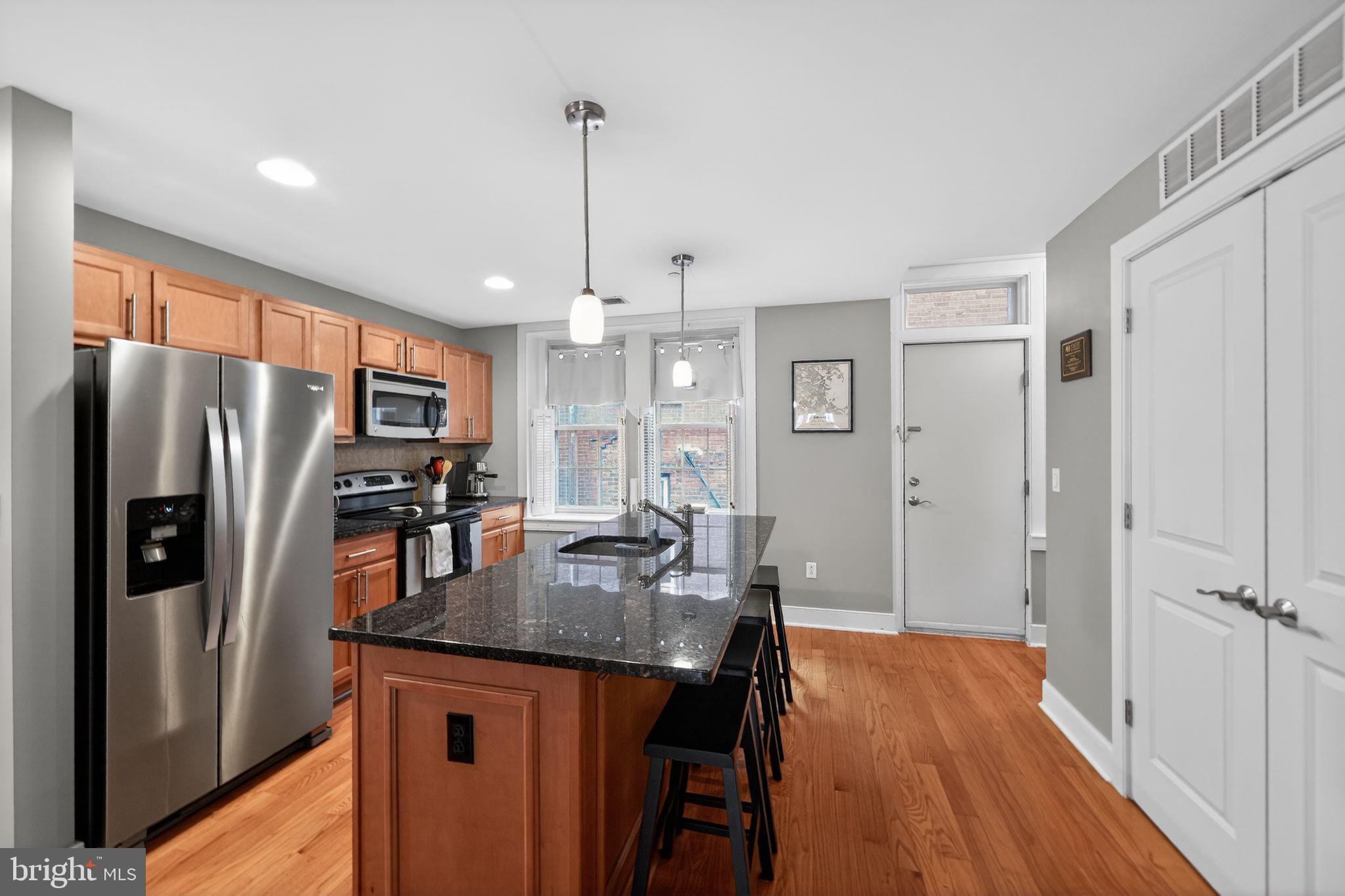 4300 Spruce Street, Unit B304 Philadelphia, PA 19104 - Photo 12 of 26 a kitchen with stainless steel appliances granite countertop a refrigerator a sink dishwasher a stove and a dining table with wooden floor