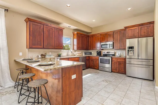 a kitchen with stainless steel appliances granite countertop a stove top oven a sink dishwasher a refrigerator and a stove with wooden cabinets