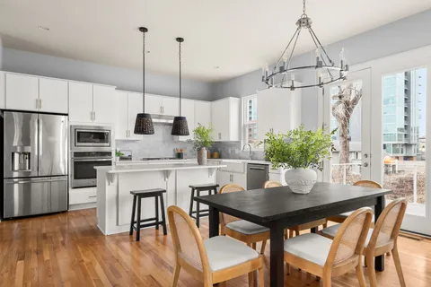 a kitchen with stainless steel appliances granite countertop a dining table chairs refrigerator and microwave