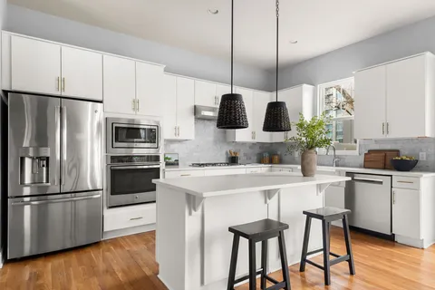 a kitchen with stainless steel appliances white cabinets a sink a stove a refrigerator and island with wooden floor