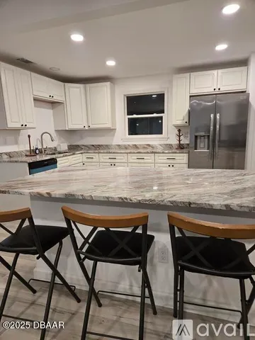 a kitchen with stainless steel appliances granite countertop a stove top oven a sink a refrigerator white cabinets and granite countertops with wooden floor