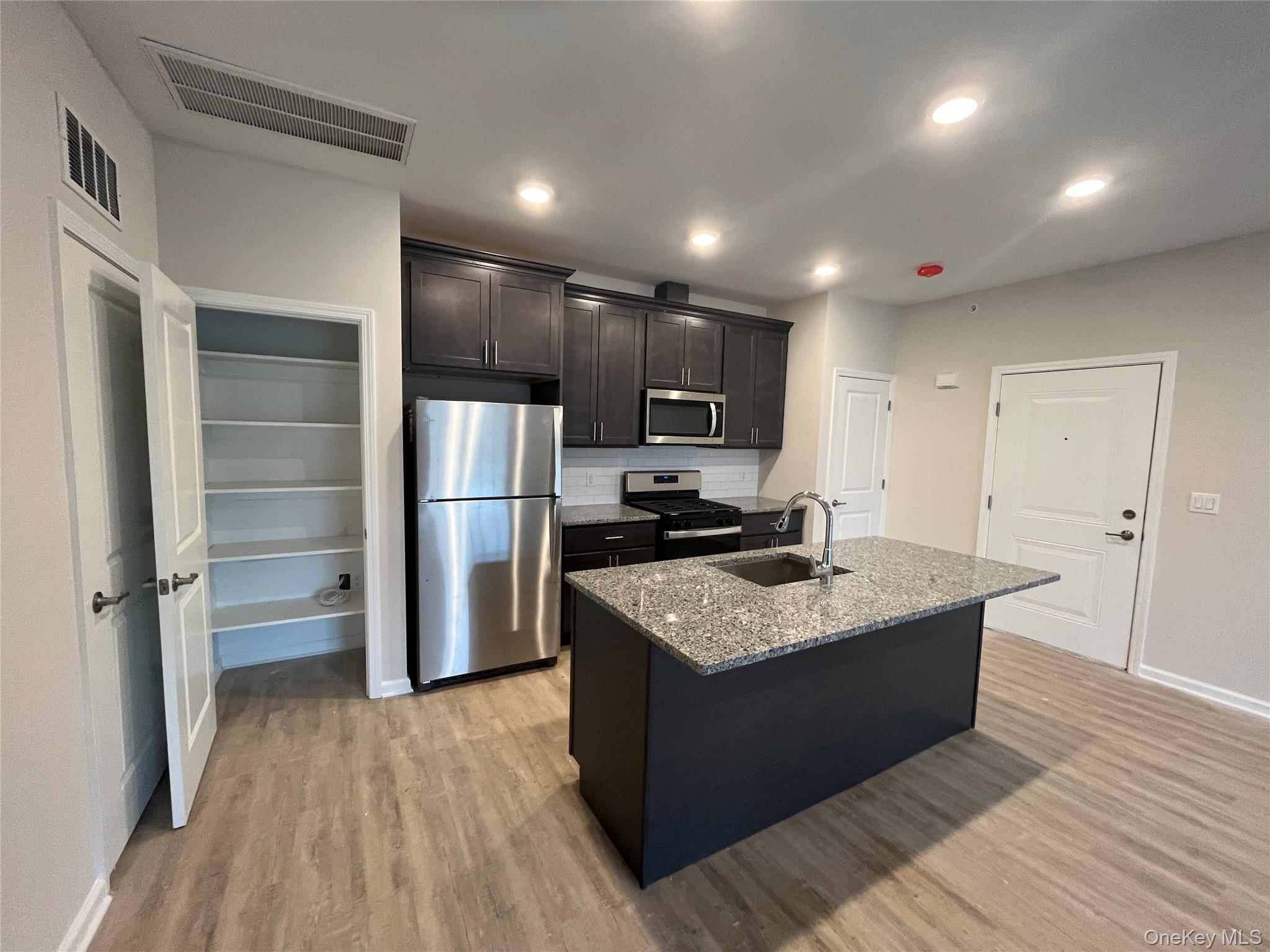 Tower Ridge Grande – Elegant open-concept kitchen with a spacious center island, stainless steel appliances, upscale cabinetry, recessed lighting pantry closet and luxury plank flooring. Designed for both style and functionality."