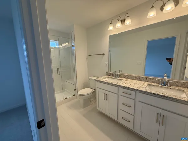 a bathroom with a granite countertop double vanity sink a mirror and a toilet