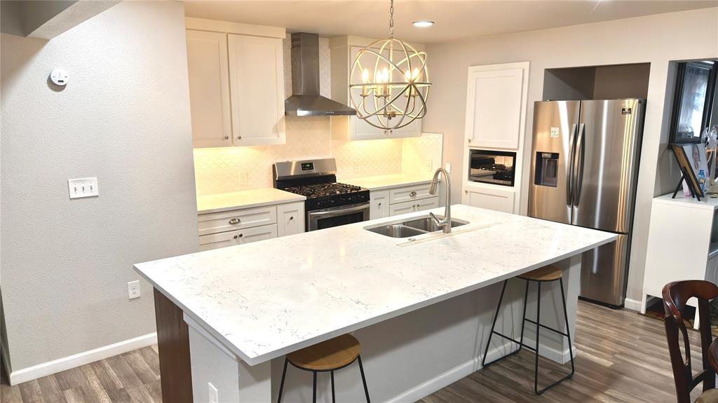 2510 Dewitt Street Irving, TX 75062 - Photo 1 of 17 Kitchen featuring stainless steel appliances, wall chimney exhaust hood, tasteful backsplash, hanging light fixtures, and a breakfast bar area