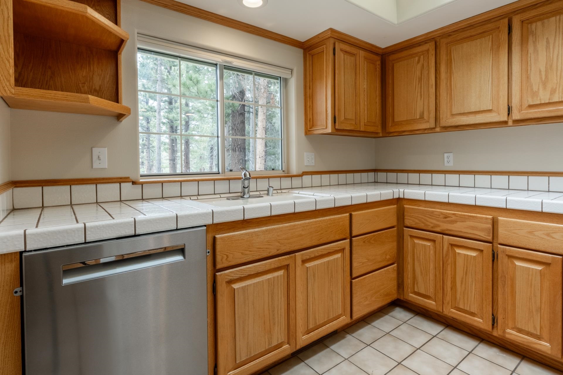 272 Ridge Way Mammoth Lakes, CA 93546 - Photo 25 of 55 Kitchen featuring extensive wood cabinetry, white tile countertops, a stainless steel dishwasher, and a window overlooking exterior trees