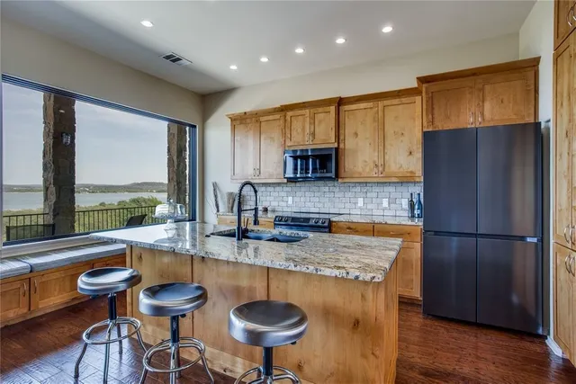 a kitchen with stainless steel appliances granite countertop a refrigerator a sink a stove a dining table and chairs