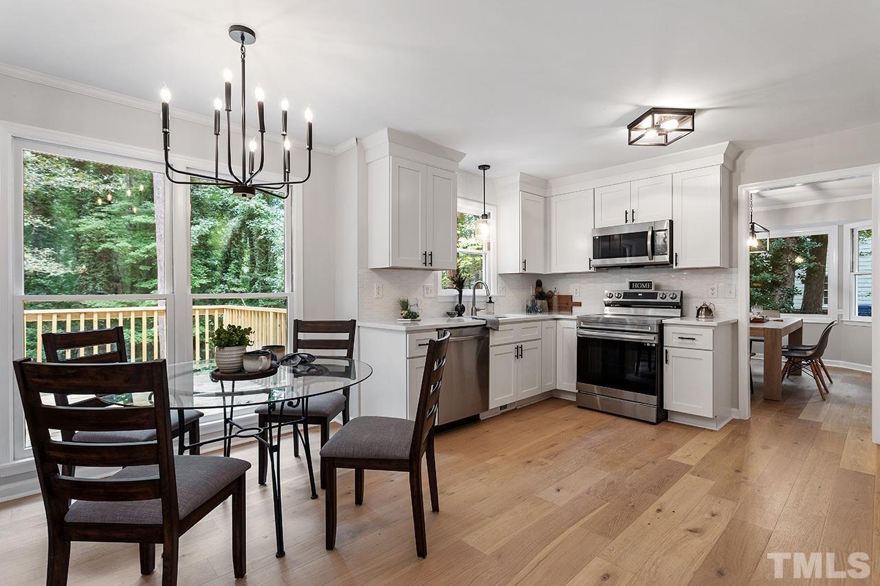 8805 Wellsley Way Raleigh, NC 27613 - Photo 2 of 39 a kitchen with stainless steel appliances a stove a sink a microwave a dining table and chairs with wooden floor