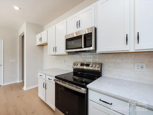 a kitchen with stainless steel appliances granite countertop white cabinets a stove a microwave and a refrigerator