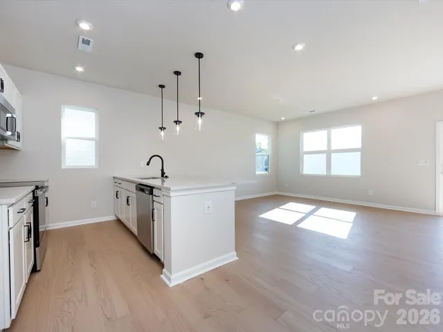 a kitchen with granite countertop a stove a sink a refrigerator and white cabinets with wooden floor