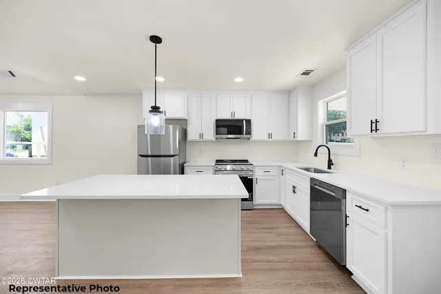 a kitchen with stainless steel appliances kitchen island granite countertop a stove a sink a refrigerator a microwave oven with white cabinets and wooden floor