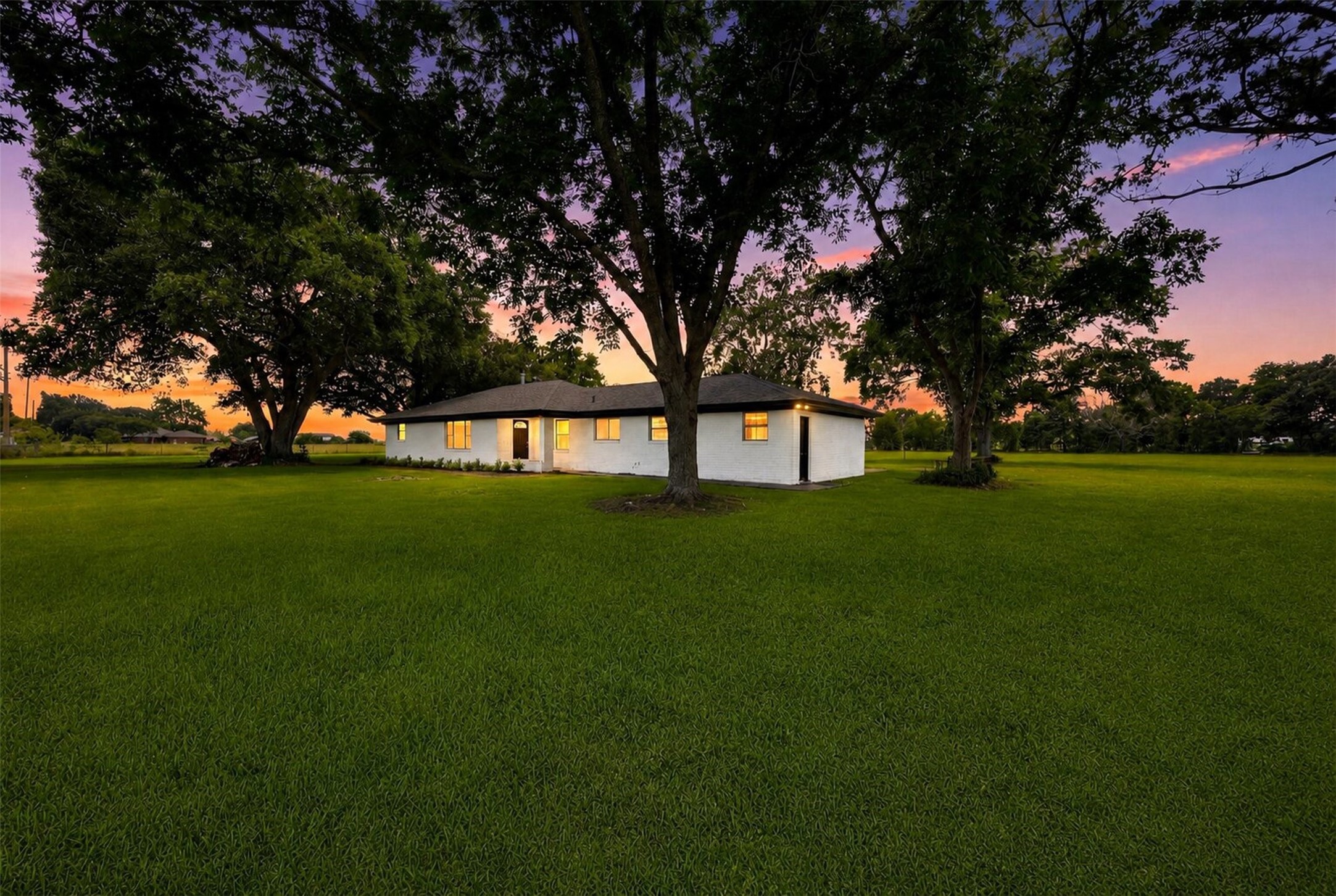 5443 Randon School Road Rosenberg, TX 77471 - Photo 1 of 20 Front elevation of a single-story white brick home set on a large, lush lawn with mature shade trees and a spacious rural backdrop.
