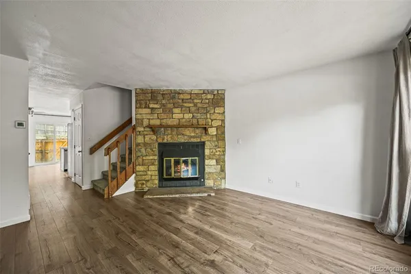a view of an empty room with wooden floor fireplace and a window