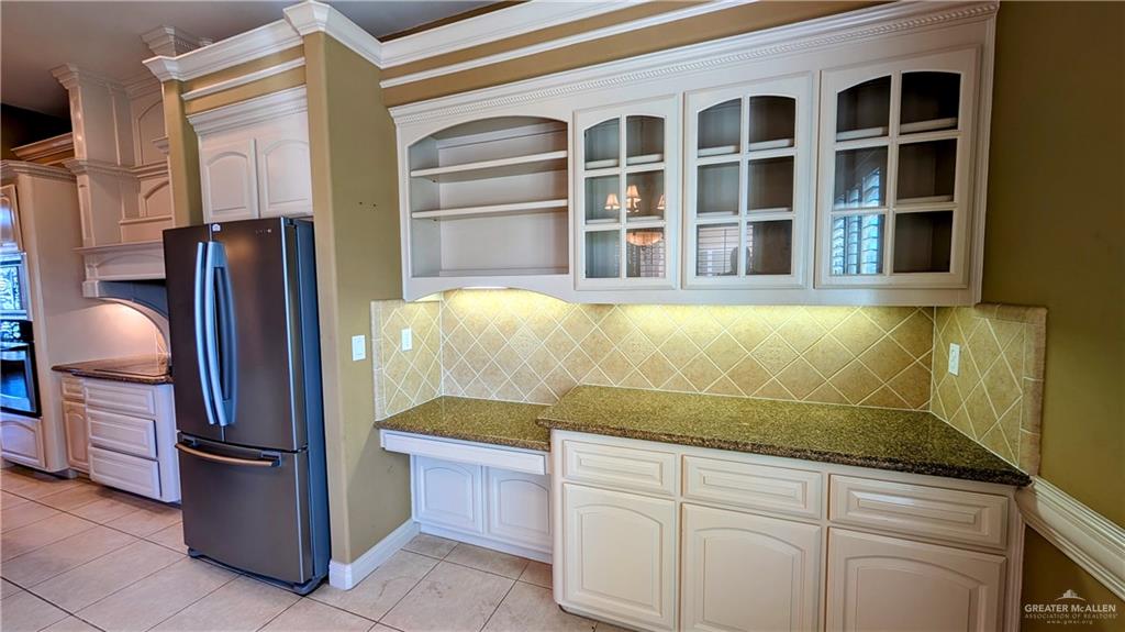 5805 Acacia Harlingen, TX 78552 - Photo 11 of 23 Kitchen with dark stone countertops, appliances with stainless steel finishes, light tile patterned flooring, ornamental molding, and glass insert cabinets