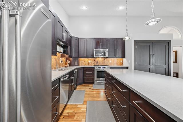 2135 Glenhill Road Colorado Springs, CO 80906 - Photo 17 of 50 Kitchen with stainless steel appliances, dark brown cabinets, hanging light fixtures, light wood-style flooring, and recessed lighting