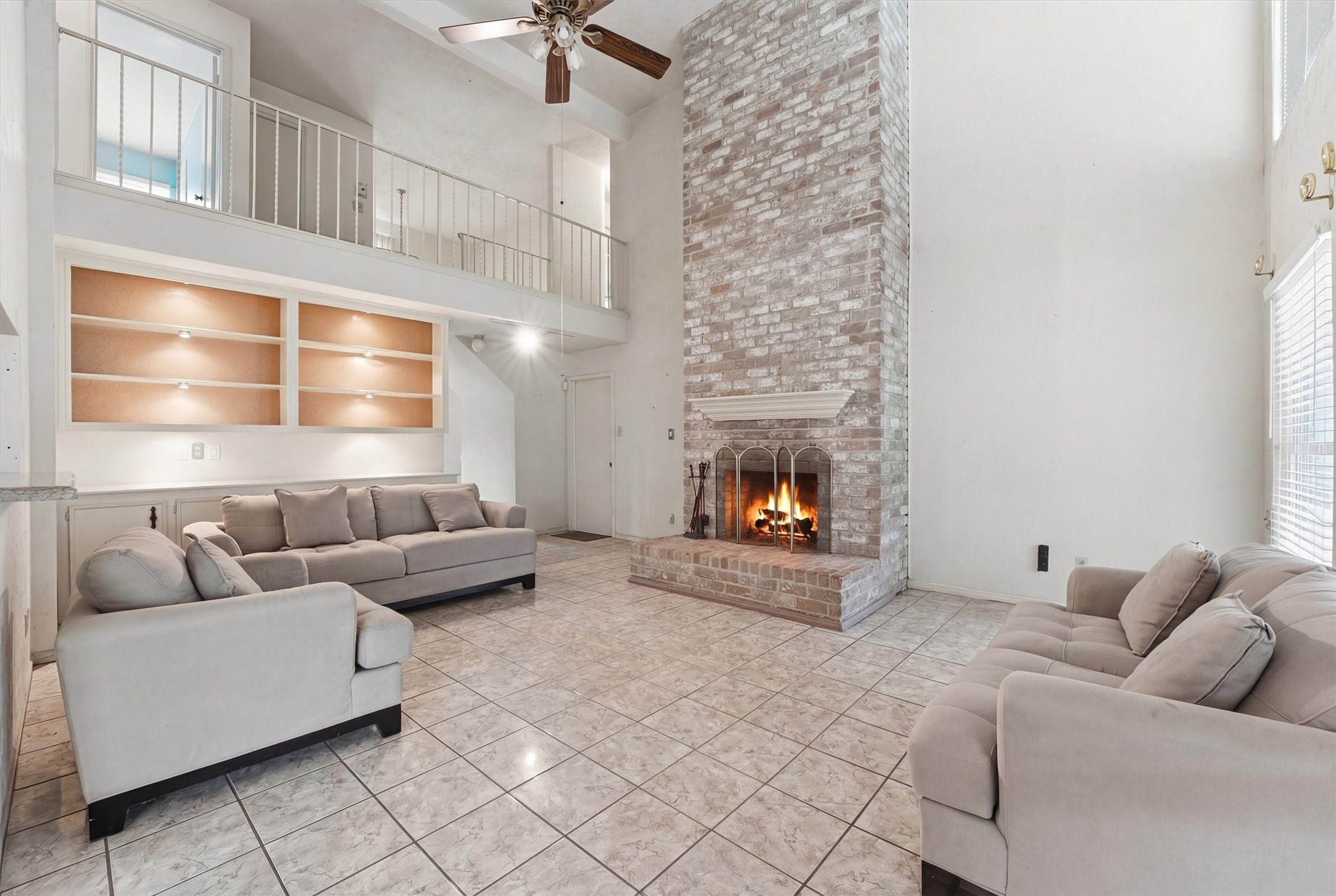 8115 Theisswood Road Spring, TX 77379 - Photo 12 of 41 high-ceiling family room showcasing the magnificent fireplace, custom built-in shelving with accent lighting, and a view of the upstairs balcony