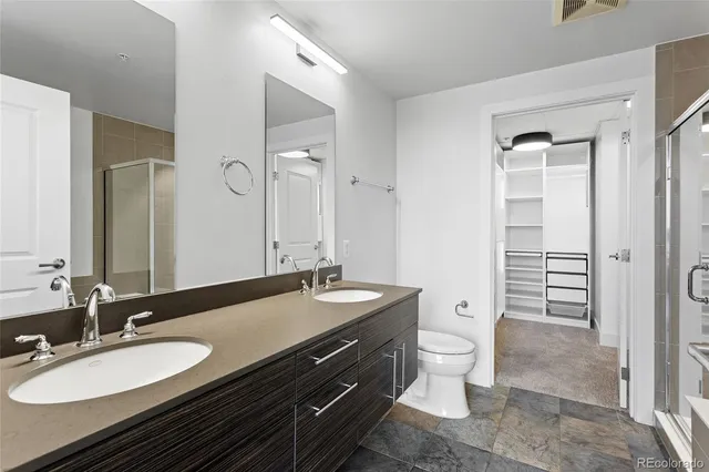 a bathroom with a granite countertop double vanity sink a mirror a toilet and a shower