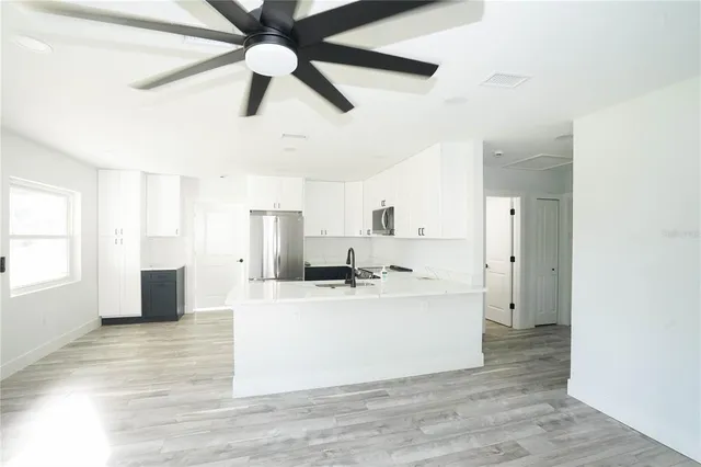 a large white kitchen with kitchen island a stove a refrigerator cabinets and a ceiling fan