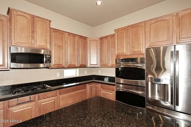 a kitchen with granite countertop a refrigerator a sink a stove top oven and cabinets