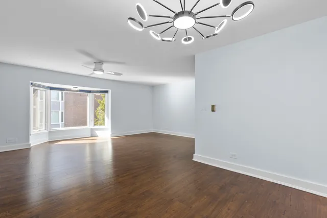 an empty room with wooden floor chandelier fan and windows