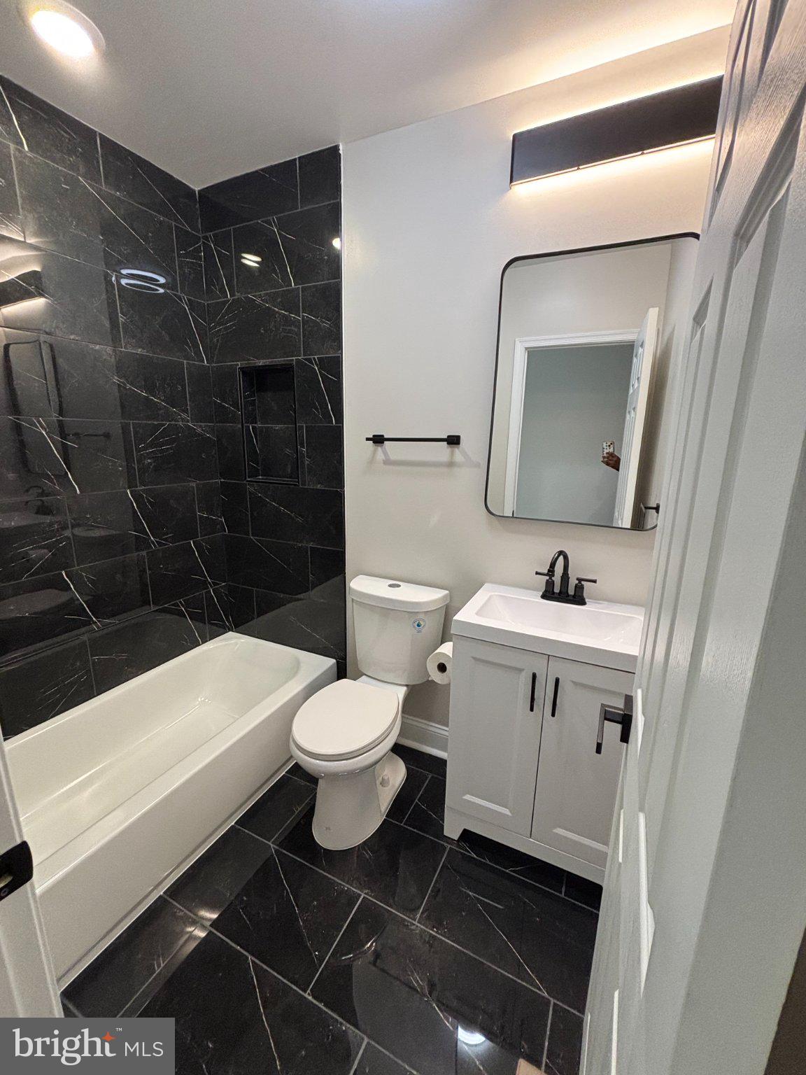4818 Pimlico Road Baltimore, MD 21215 - Photo 15 of 18 a bathroom with a toilet a sink a mirror and a bathtub