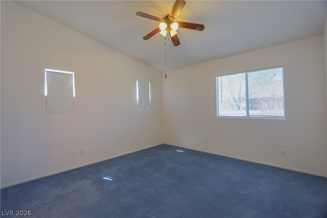 6472 Centennial Road Pahrump, NV 89048 - Photo 5 of 29 A quiet bedroom with a ceiling fan and a soft carpet, bathed in natural light from ample windows.