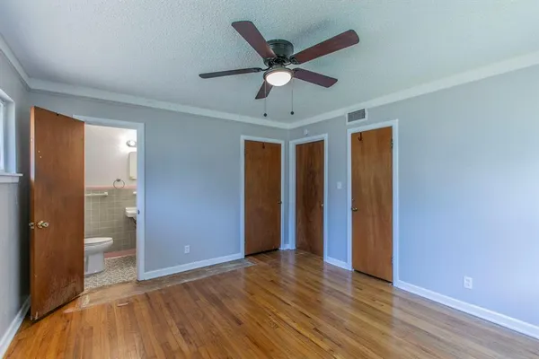 a view of an empty room with wooden floor and a ceiling fan