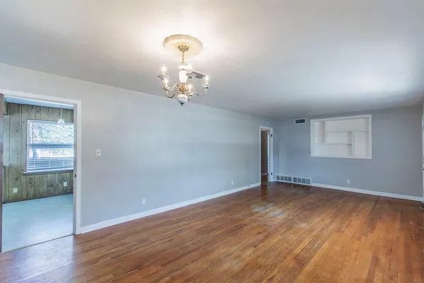 an empty room with wooden floor mirror and windows