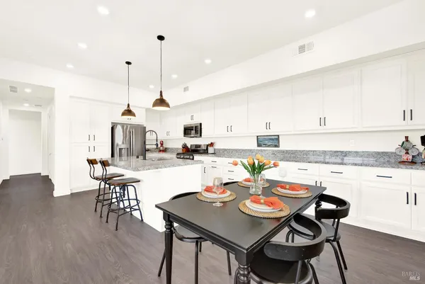 a kitchen with stainless steel appliances kitchen island granite countertop a dining table chairs and white cabinets