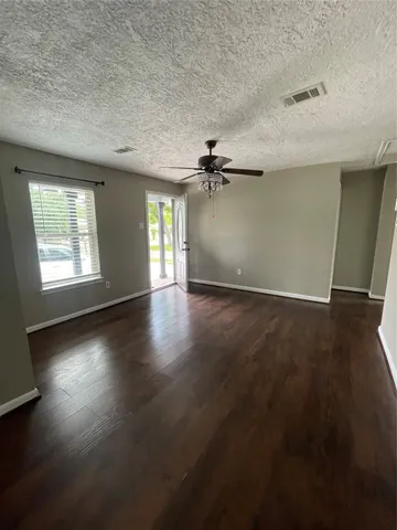 an empty room with wooden floor fan and windows
