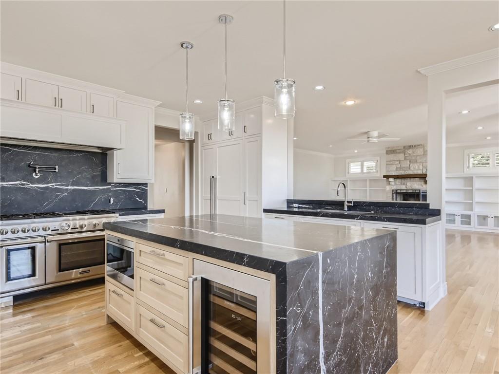 267 North Commons Ford Road Austin, TX 78733 - Photo 1 of 34 Kitchen with ornamental molding, a kitchen island, a stone fireplace, light wood-style floors, and wine cooler