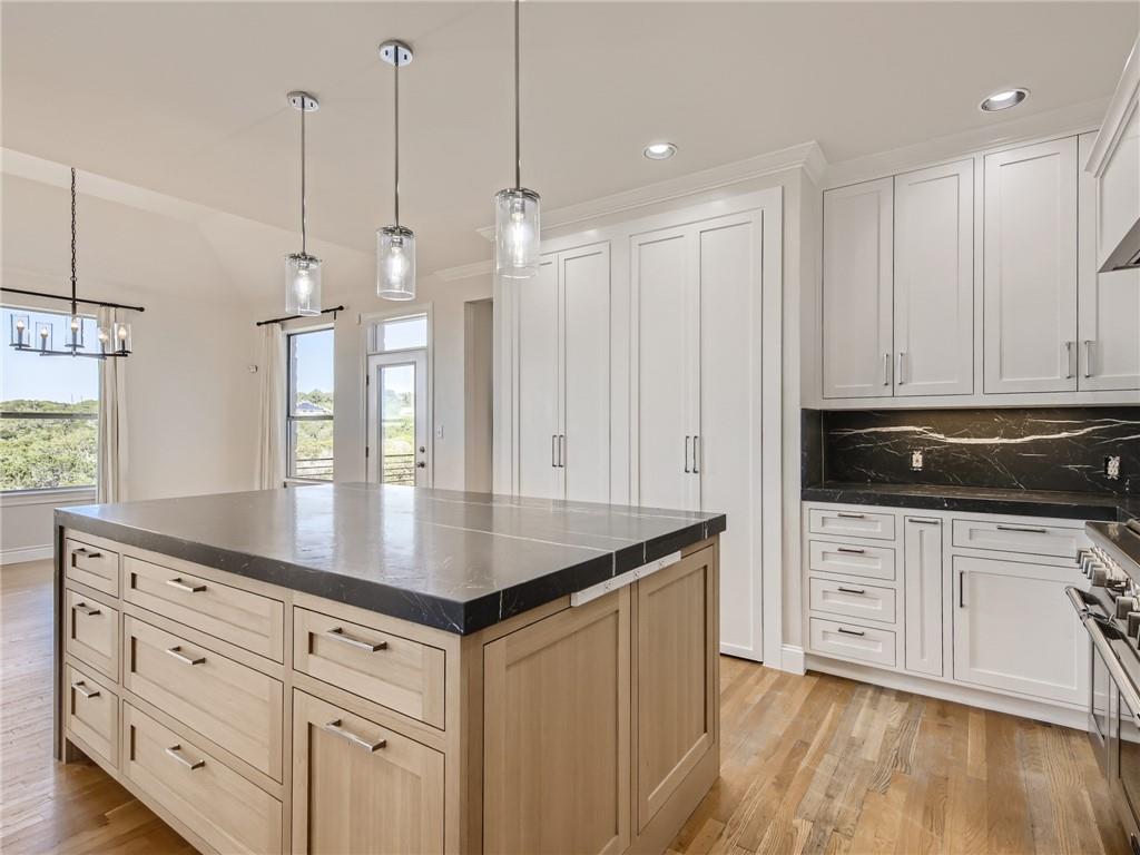 267 North Commons Ford Road Austin, TX 78733 - Photo 8 of 34 Dual tone kitchen with decorative backsplash, light wood-style flooring, range with two ovens, decorative light fixtures, and a kitchen island