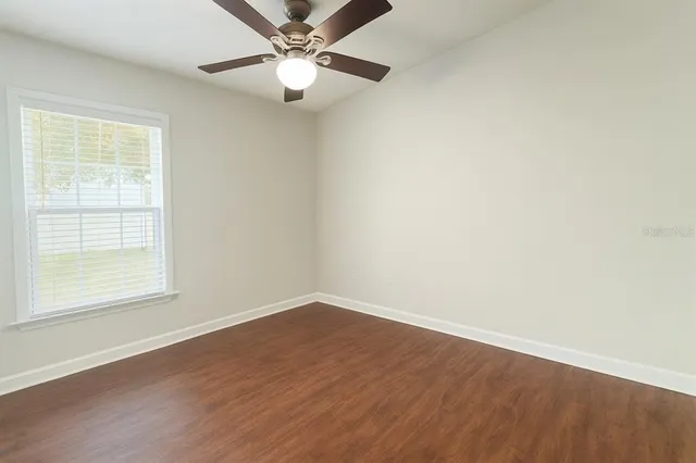 an empty room with wooden floor fan and windows