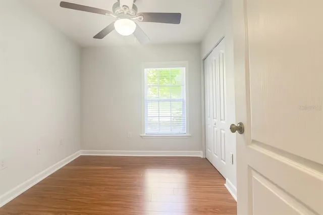 an empty room with wooden floor fan and windows