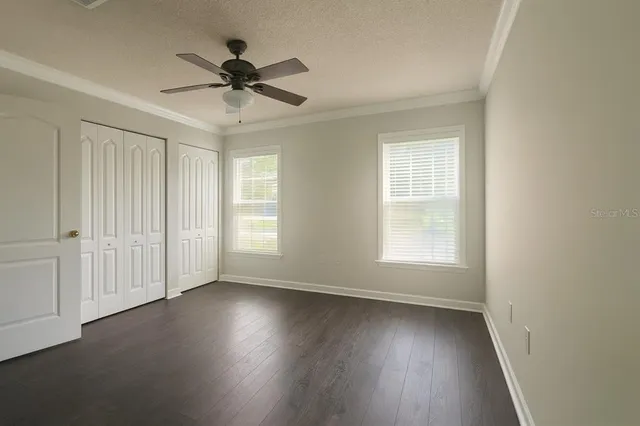an empty room with wooden floor fan and windows